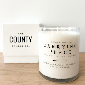 Carrying Place hand-poured cedar wood, palo santo, and sandalwood premium soy candle in a clear glass jar, made by The County Candle Co.  Hand-poured and made from 100% premium soy wax, cotton wicks, and phthalate-free fragrances infused with essential oils, we pride ourselves on creating luxurious candles using time-honored technique and eco-conscious materials. Made in Prince Edward County, Ontario, Canada. 